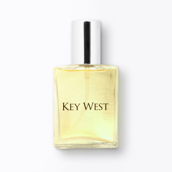 A clear rectangular cologne bottle with a shiny silver cap is shown against a white background. The liquid inside is a light yellow color, and the label reads "Key West."